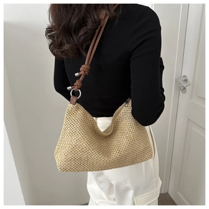 Detail of woven straw hobo bag featuring brown leather shoulder strap with knot detail