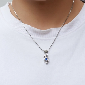 Detailed view of silver owl pendant with blue gemstone worn on a box chain