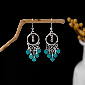 Detail of bohemian turquoise drop earrings with silver metal rings on a wooden branch