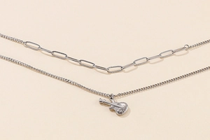 Detailed view of a silver double-layered necklace featuring a sleek guitar pendant and clip chain