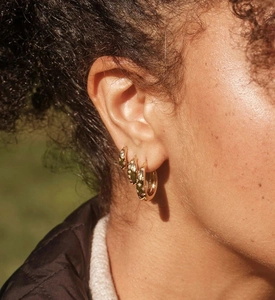 Close-up of gold star-engraved hoop earrings in three sizes worn on a woman ear