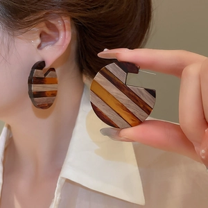 Detail of striped geometric C-shape earrings in brown and beige colors worn by model