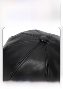 Detailed top view of a black PU leather baker boy hat showing stitched panel and central button