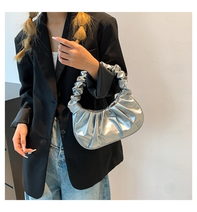 Silver pleated dumpling bag with metallic finish held by model in a minimalist setting