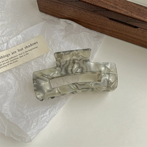 Top view of square grey marble acetate hair claw clip on clean white paper backdrop