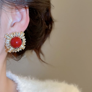 Close-up of elegant gold stud earring with a large red bead and sparkling crystals