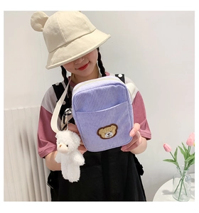 Lavender corduroy crossbody bag featuring a bear patch and plush charm on a model