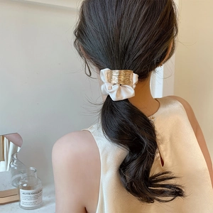 Chouchou chic avec arche métallique dorée et tissu plissé blanc sur une queue de cheval