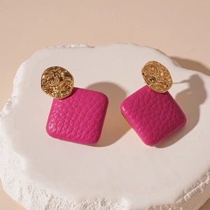 Close-up of geometric earrings featuring hammered gold metal and magenta leather texture