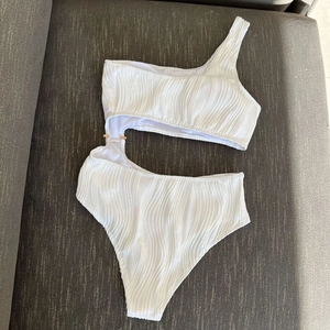 Detailed close-up of white textured fabric and gold metal ring on a cut-out swimsuit