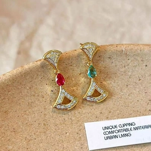 Macro detail of asymmetric 14K gold plated fan and teardrop earrings with red and green stones
