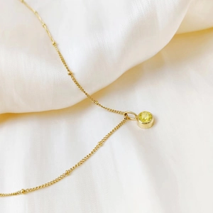 Macro view of gold beaded chain with round yellow birthstone pendant on silk fabric