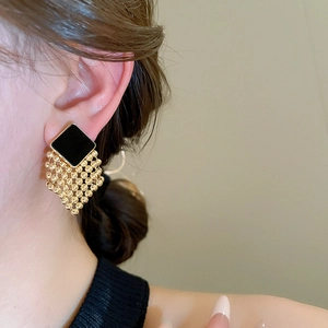 Detail of woven diamond earrings with black enamel square and golden bead tassels