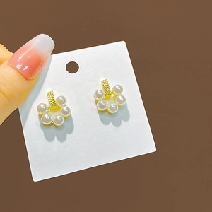 Detail of floral pearl earrings with gold petals held against a brown background