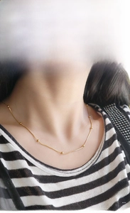 Detail of 18K gold snake chain necklace with gold beads worn on neck for a minimalist look