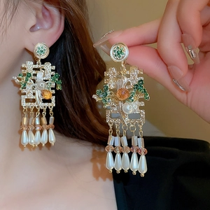 Close-up of golden phoenix ear clips with green enamel, Xi character, and pearl tassels