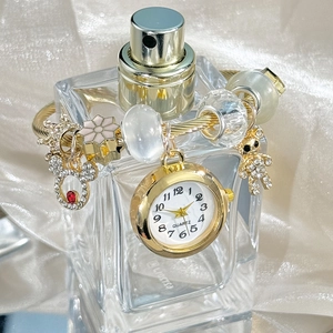 Detail of golden charm bracelet watch featuring a quartz dial and crystal bear pendant