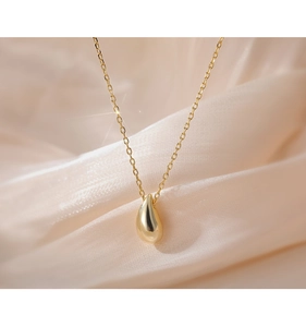 Close-up of polished gold teardrop pendant on minimalist fine chain over beige silk