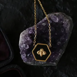 Macro shot of hexagonal honeybee pendant with black enamel on purple crystal cluster