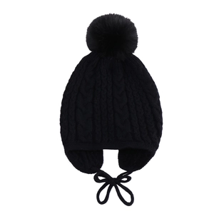 Detail of black cable knit baby winter hat with large faux fur pompom and earflap straps