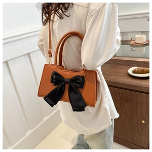 Detail view of a brown leather handbag with a large black bow, shown on a model
