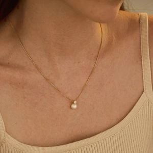 Elegant gold stainless steel necklace featuring a white pearl and zircon stone on a model