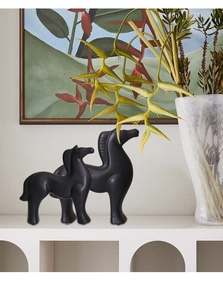 Set of two modern matte black horse sculptures on a white cabinet in a cozy home setting