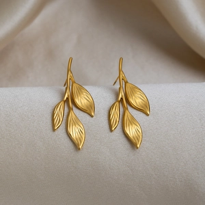 Macro shot of gold leaf earrings with polished finish on soft beige fabric texture