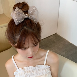 Detail of a grey mesh bow hair scrunchie with rhinestones worn on a model hair bun
