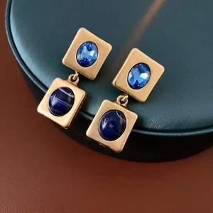 Detailansicht von Vintage-Goldohrringen mit blauen Steinen auf grünem Ständer