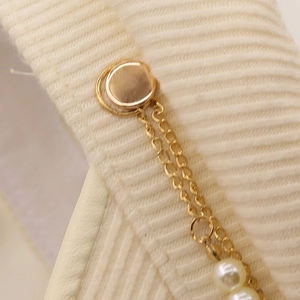 Detail of gold chain and pearl accent on beige corduroy fabric for sailor cap