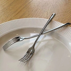 Detail of two silver stainless steel fruit forks on a white ceramic plate and wooden desk