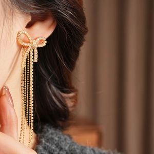 Detail of 18k gold plated bow tassel earrings featuring sparkling zircon on a model