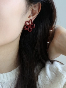 Nahaufnahme der roten hohlen Blumenohrringe am Modell mit eleganten floralen Blütenblattdetails