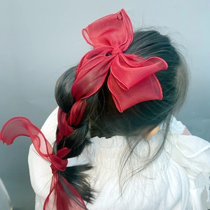 Detail of a red organza bow hair clip woven into a braided hairstyle for girls