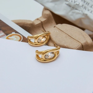 Detailed close-up of golden C-shaped stainless steel earrings with large oval zircon stone