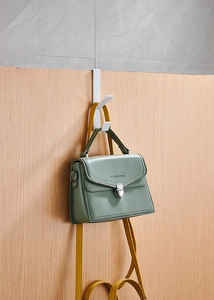 White double door hook holding a light green leather handbag against a wooden door
