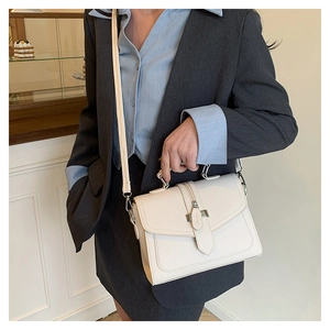 Detail view of white leather crossbody bag with top handle and metallic buckle closure
