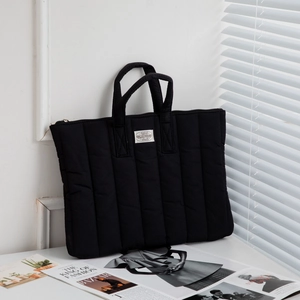Detail of black quilted laptop bag with soft padding and woven handles on a desk