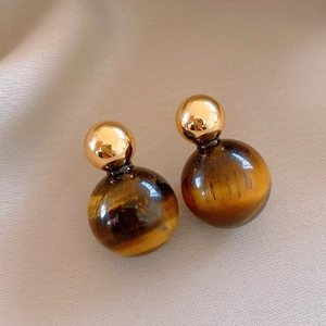 Macro view of gold metal and tiger eye stone double ball stud earrings on beige fabric