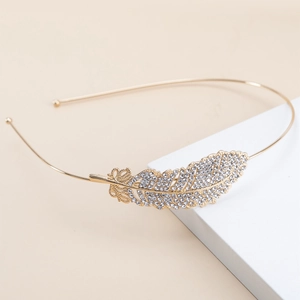 Elegant gold feather metal headband with sparkling rhinestones on white cube pedestal