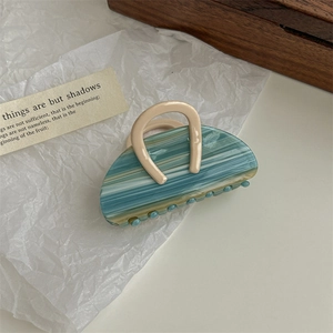 Detail showing marble texture acetate hair claw clip with green and blue patterns