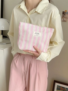 Pink and white striped fabric makeup bag with a minimalist design held by a model