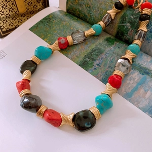 Detail of vintage beaded necklace with red coral, turquoise, and gold spacers on book