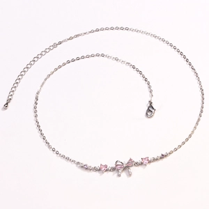 Detail of silver O-chain necklace featuring pink heart stone and zirconia bow pendant