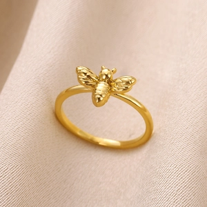 Gros plan détaillé d'une bague abeille dorée sur tissu rose montrant les ailes fines