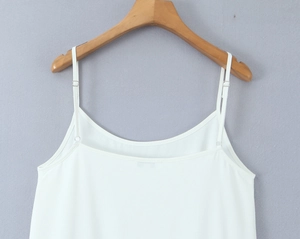Détail de la robe blanche à fines bretelles avec tissu drapé suspendue sur un cintre en bois