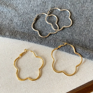 Detailed view of gold and silver minimalist flower-shaped large hoop earrings on fabric