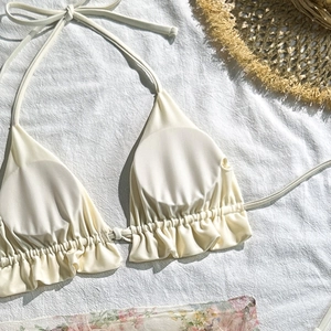 Close-up of cream halter bikini top with ruffle trim on natural linen background