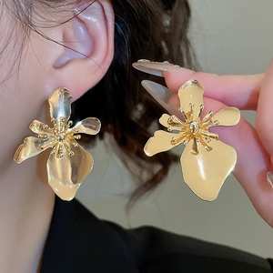 Macro shot of oversized gold flower earrings featuring a polished metallic textured finish